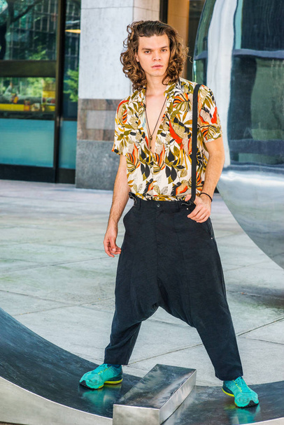 Young American Artist with brown curly hair in New York, wearing colorful patterned short sleeve shirt, baggy loose pants, one suspender on shoulder, patterned sneakers, hanging old key as necklace - Photo, Image