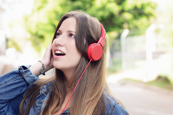 Portrait of young beautiful woman with red headphones listening music. Outdoors. Urban concept. - 写真・画像
