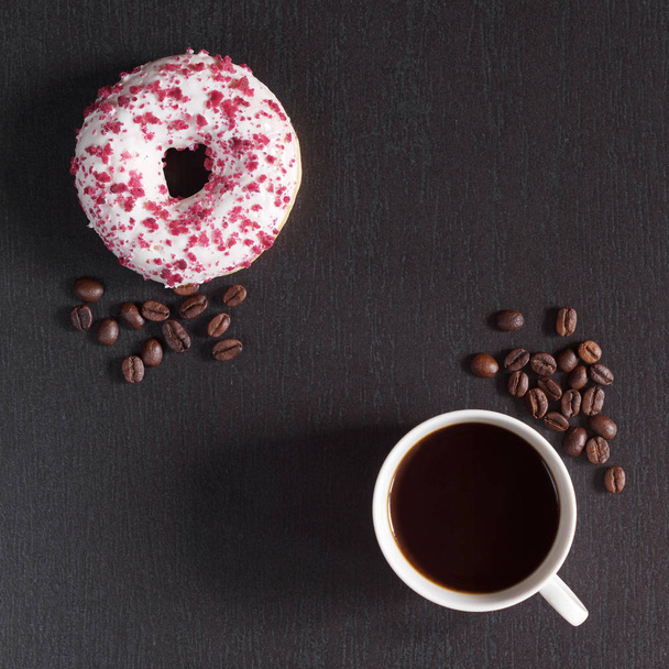 Xícara de café e um doce donut com creme de coalhada decorado com migalhas de frutas vermelhas contra um fundo de pedra preta, vista superior
 - Foto, Imagem
