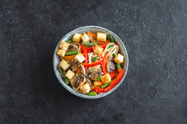 Stir fry with udon noodles, tofu, mushrooms and vegetables. Asian vegan vegetarian food, meal, stir fry over black background, copy space. - Фото, изображение
