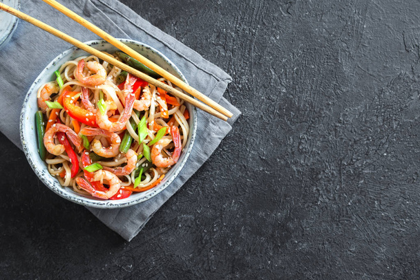 Stir fry with udon noodles, shrimps (prawns) and vegetables. Asian healthy food, meal, stir fry in bowl over black background, copy space. - Photo, Image