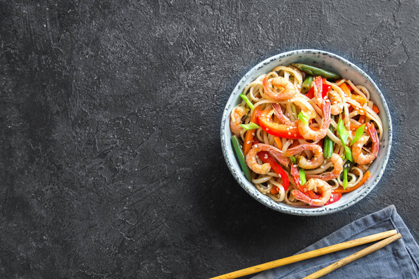 Stir fry with udon noodles, shrimps (prawns) and vegetables. Asian healthy food, meal, stir fry in bowl over black background, copy space. - Photo, Image