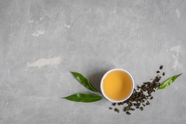 Green tea in ceramic cup, dry green oolong tea and tea leaves on grey stone table, top view, copy space. - Фото, зображення