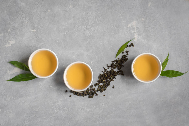 Green tea in ceramic cup, dry green oolong tea and tea leaves on grey stone table, top view, copy space. - Photo, image