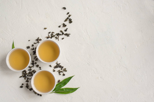 Green tea in ceramic cups, dry green oolong tea and tea leaves on white stone table, top view, copy space. - Foto, afbeelding