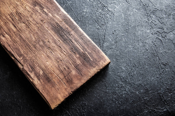 Rustic wooden cutting board on black stone background close up - rustic empty copy space for text, design element - Φωτογραφία, εικόνα