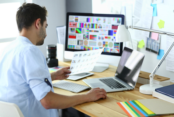 Портрет молодого дизайнера, який сидить у графічній студії перед ноутбуком та комп'ютером під час роботи в Інтернеті
. - Фото, зображення