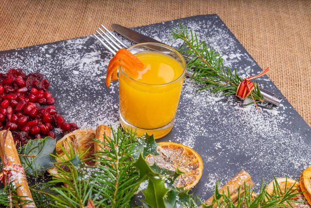 Χριστούγεννα σχιστόλιθος πιατέλα. Διακοσμημένα Slate Platter, με ένα ποτήρι παγωμένο χυμό πορτοκάλι, έτοιμο για εορταστική φαγητού για να σερβίρουμε. - Φωτογραφία, εικόνα