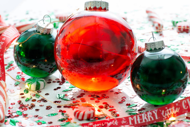 赤い液体が付いている装飾いっぱいクリスマス飾りボールと赤いがある自分のメリー クリスマス リボン、クリスマス ライト、ペパーミント ・ キャンディのセットに囲まれた 2 つの緑いっぱい飾りボール - 写真・画像