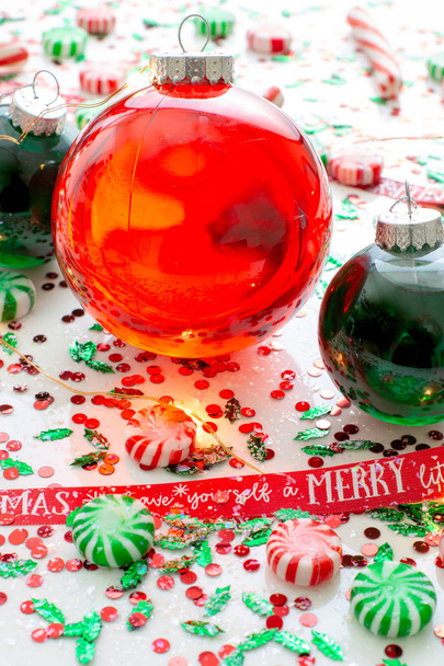 Украшение с красной жидкостью заполнены Рождественский орнамент шар и два зеленых заполненных орнамент шары в окружении красного Have Yourself Веселый Рождественская лента, набор рождественских огней и мяты конфеты
 - Фото, изображение
