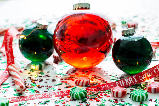 Decoratie met rode vloeistof gevuld Christmas ornament bal en twee groene gevulde sieraad ballen omringd door een rode Have Yourself A Merry Christmas lint, een set van kerstverlichting en pepermunt snoep - Foto, afbeelding