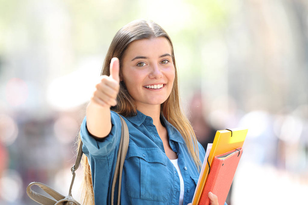 Portrait of a happy student in the street with thumb up with a blurred background - Fotó, kép