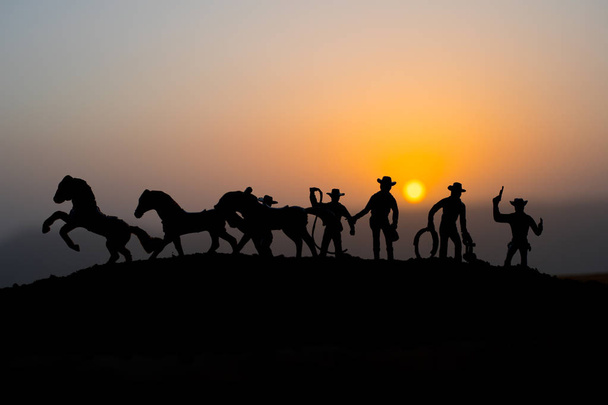 Έννοια καουμπόη. Σιλουέτα του καουμπόηδες κατά το ηλιοβασίλεμα. Καουμπόηδες σιλουέτες σε ένα λόφο με άλογα. Επιλεκτική εστίαση - Φωτογραφία, εικόνα