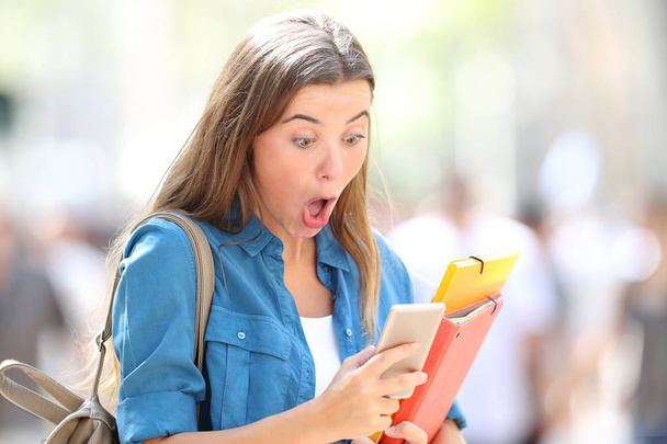 Surprised student receiving good online news in the street - Foto, afbeelding