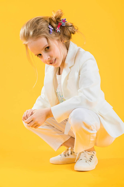 A teenage girl in white clothes is squatting on a yellow background. - Foto, imagen