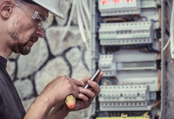a male electrician works in a switchboard with an electrical connecting cable, connects the equipment with tools, the concept of complex work, space for text - Photo, Image