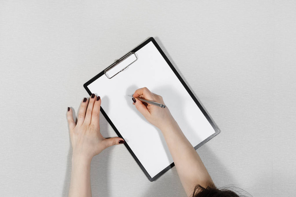 Woman writes on blank white sheet of paper. Clipboard in female hands. Flat lay. - Photo, Image