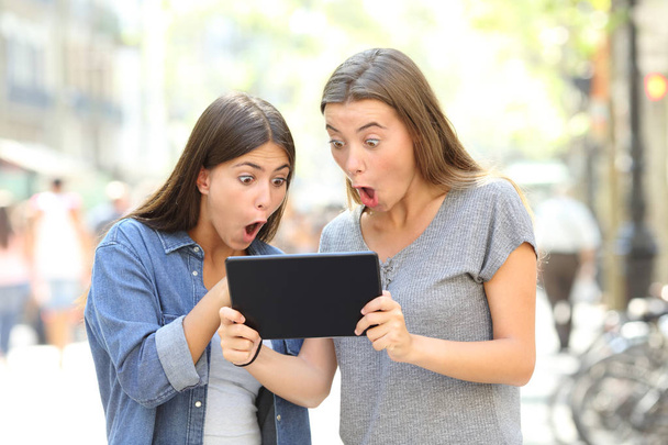 Two surprised friends finding online content in a tablet in the street - Foto, immagini