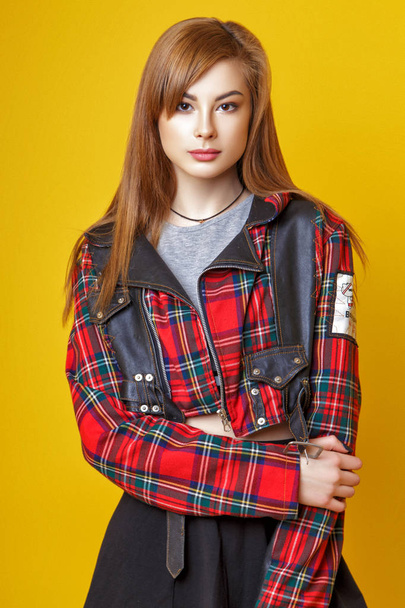 A cute young Asian girl with red hair, dressed in a plaid jacket, skirt and leggings posing in the studio on a yellow background. - Photo, Image