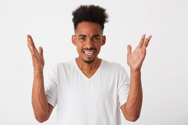 Gros plan de jeune homme afro-américain en colère avec les cheveux bouclés et les mains levées porte t-shirt se sent irrité et argumenter isolé sur fond blanc
 - Photo, image