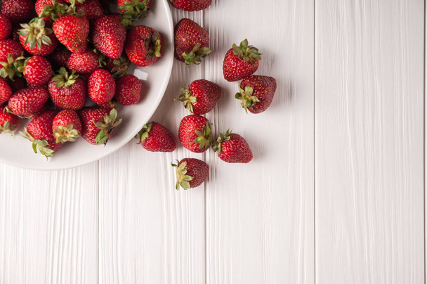 Fresas frescas en un plato sobre un fondo de madera blanca
 - Foto, imagen