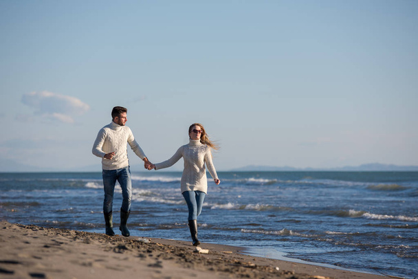 Young couple having fun walking and hugging on beach during autumn sunny day - Foto, afbeelding