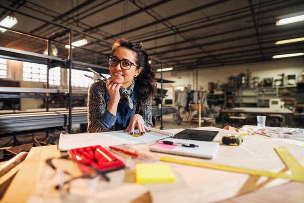 улыбающаяся профессиональная женщина-архитектор с записками, планшетным ПК и линейками в мастерской
 - Фото, изображение