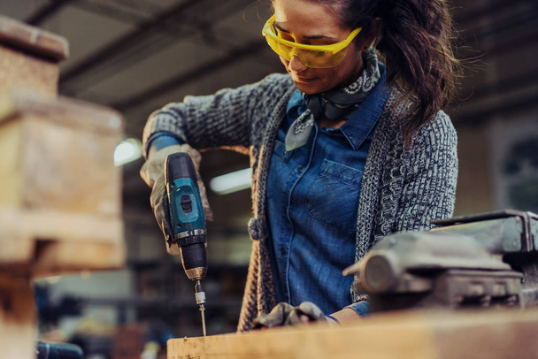  профессиональный плотник-женщина, работающая с электродрелью в мастерской
 - Фото, изображение