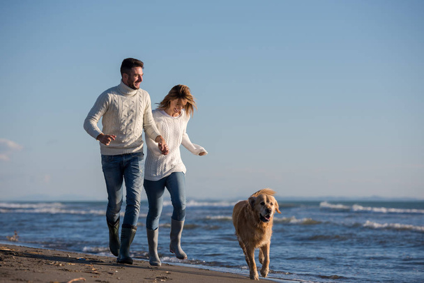 Couple Running On The Beach Holding Their Hands with dog On autmun day - Valokuva, kuva
