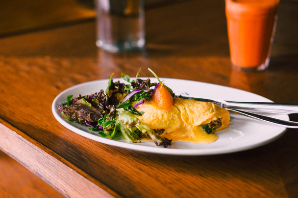 Rano śniadanie, omlet z zieloną sałatą na białe płytki z świeże marchewki pomarańczowy sok. Drewniany stół. Fotografii żywności, koncepcja blogów. - Zdjęcie, obraz