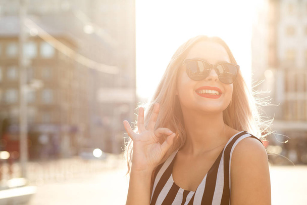 Urban portrait of glamor cheerful woman in glasses showing ok gesture, enjoying summer day. Empty space - Photo, Image
