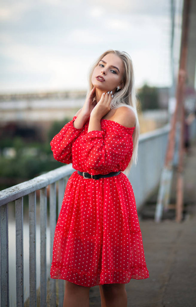 Tender blonde woman wearing trendy red dress, posing on the bridge in the evening - Photo, Image