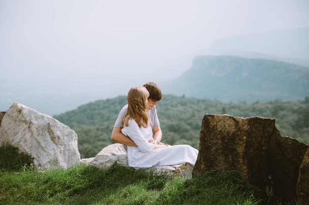 Młoda para siedzi na skraju gór z pięknym widokiem - Zdjęcie, obraz