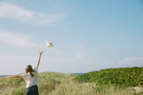 schöne junge Frau wirft Hut in die Luft, Sommerlandschaft - Foto, Bild