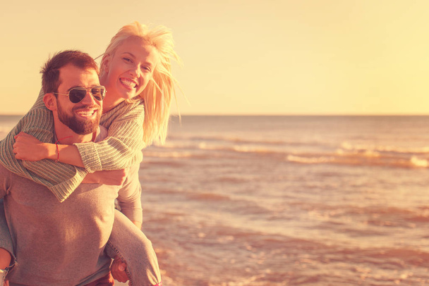 Men Giving Piggy Back Rides to his girlfriend At Sunset By The Sea, autumn time - Foto, Imagem