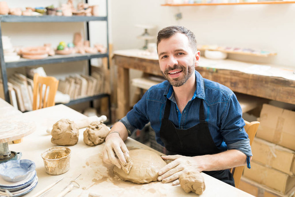 Portrait of confident man shaping clay with sponge in pottery class - Photo, Image
