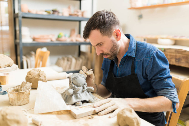 Propriétaire masculin confiant faisant la sculpture d'argile de poupée à l'établi dans l'atelier
 - Photo, image