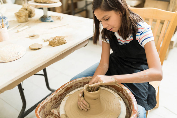 Cute female student wheel throwing while sitting in pottery class - Photo, Image