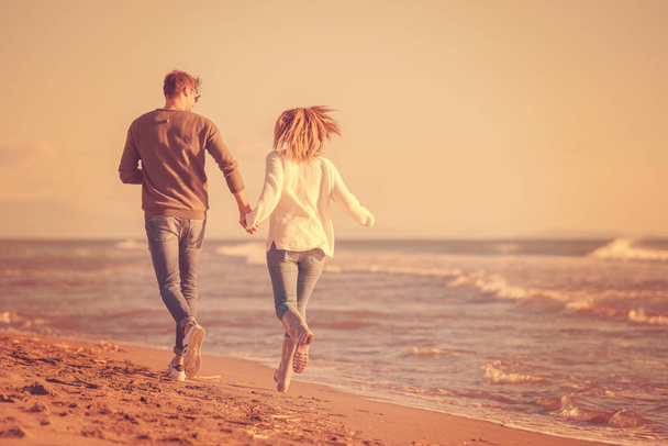 Young couple having fun walking and hugging on beach during autumn sunny day - Foto, Imagem