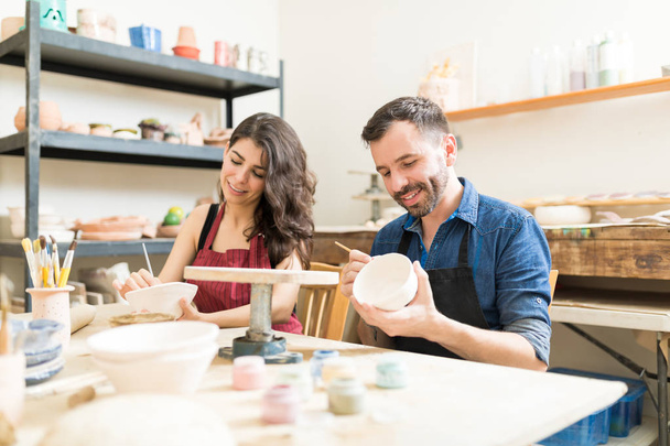 Couple adulte moyen souriant tout en faisant de la peinture créative sur des bols en atelier de poterie
 - Photo, image