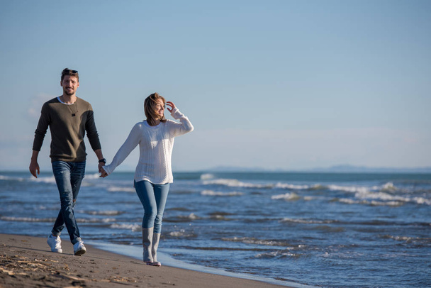 Young couple having fun walking and hugging on beach during autumn sunny day - Fotó, kép