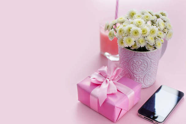 Σύνθεση επίπεδη lay δώρο για μια γυναίκα. Σύγχρονο gadget κινητό τηλέφωνο ποτήρι κοκτέιλ άρωμα μπουκέτο λουλούδια. Προετοιμασία για το κουτί δώρο έκπληξη διακοπές. ροζ φόντο - Φωτογραφία, εικόνα