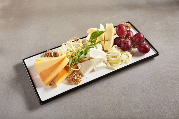 Wine Plate with Cheese Mix, Nuts and Grapes on White Rectangular Flat Plate. Cheeseboard with Pieces of Various Cheese such as Cheddar, Manchego, Gauda and Smoked Cheese - Fotoğraf, Görsel