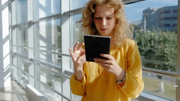 Young beautiful business woman, by the window with a tablet - Felvétel, videó