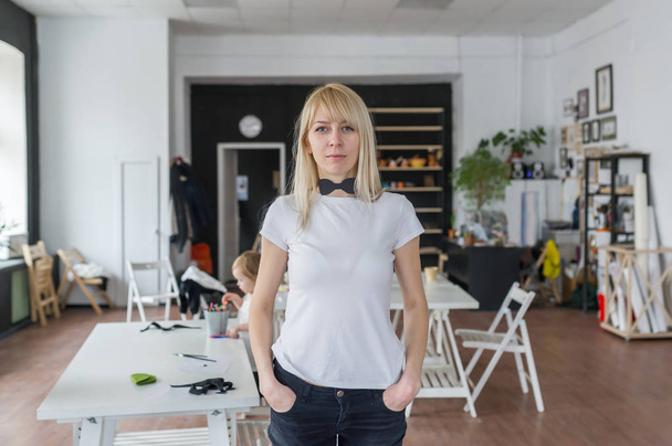 Portrait de la jeune femme blonde avec des émotions heureuses dans un studio créatif.L'enfant litlle assis à une table à l'arrière-plan
 - Photo, image