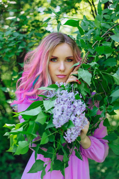 Beautiful girl with colorful dyed hair and perfect makeup standig next to lilac bush - Foto, Imagen