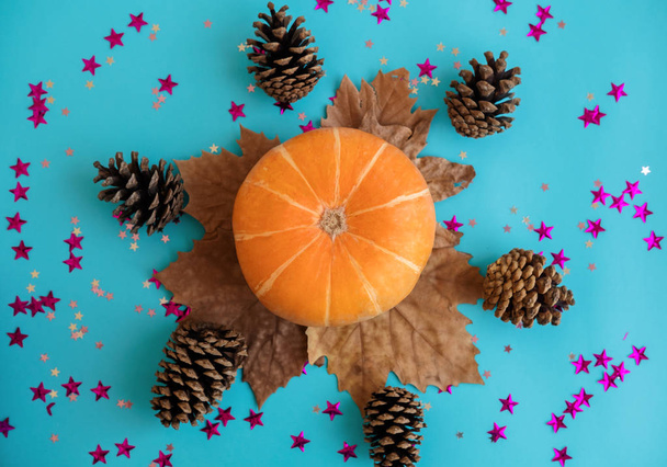 Orange pumpkin lies on blue background with leaves and cones. Concept of autumn, Thanksgiving, Halloween. Top view. Flat lay. - Fotó, kép