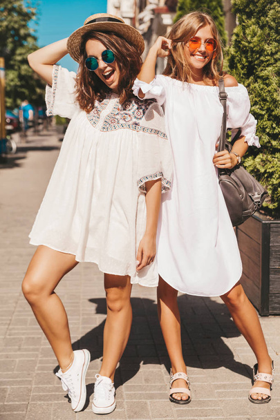 Fashion portrait of two young stylish hippie brunette and blond women models in summer sunny day in white hipster clothes posing on the street background. Going crazy - Fotografie, Obrázek