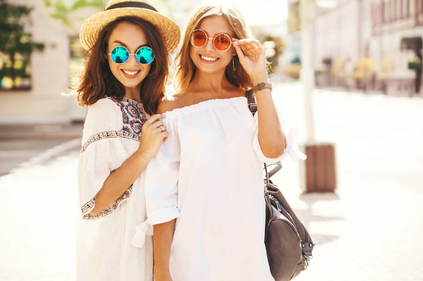 Fashion portrait of two young stylish hippie brunette and blond women models in summer sunny day in white hipster clothes posing on the street background. Going crazy - Fotó, kép