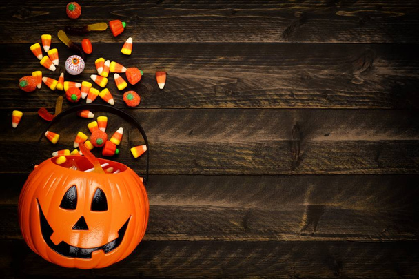 Halloween Jack o Lantern emmer met zijrand van het morsen van snoep. Boven weergave op een rustieke houten achtergrond met kopie ruimte. - Foto, afbeelding